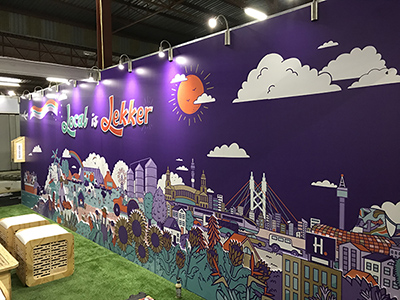 A wall branded by Hollard at Nampo with urban and agricultural illustration and text reading "local is lekker".