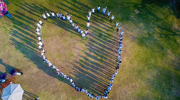 A group of people standing together forming a heart-shape.