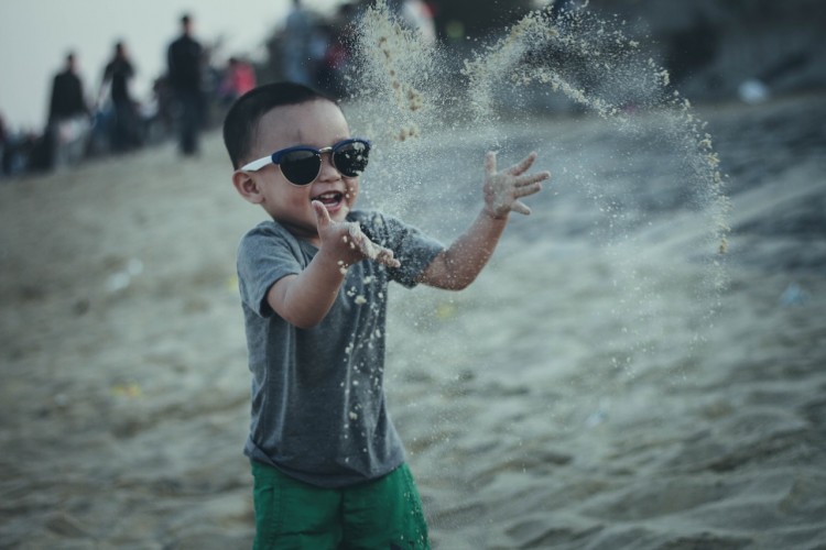 A little boy throwing beach sand in the air, laughing.