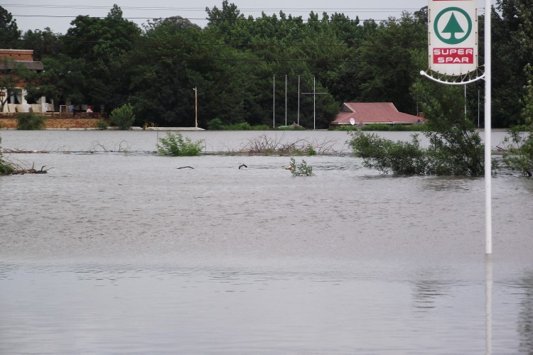 A flooded residential area with the roofs of houses barely visible and a sign-post in the foreground.