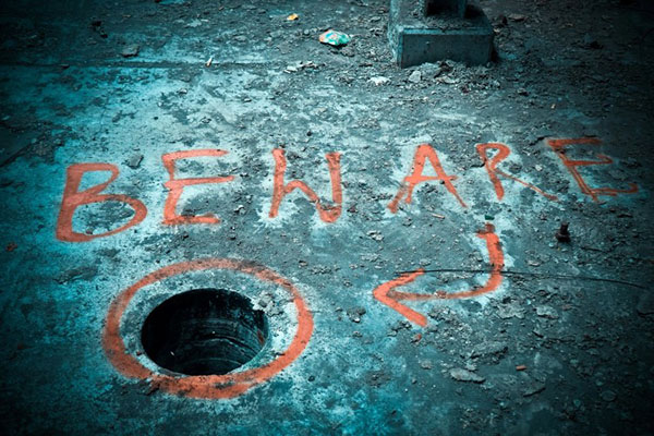 Hole in the ground with a red circle drawn around it and the word "beware" written in spray-paint just above.