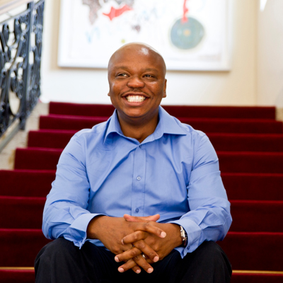 Hollard CEO Saks Ntombela smiling while sitting on a staircase at Hollard's Parktown Campus