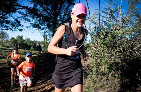 Lady competitor in a pink cap running through the mountains followed by two children